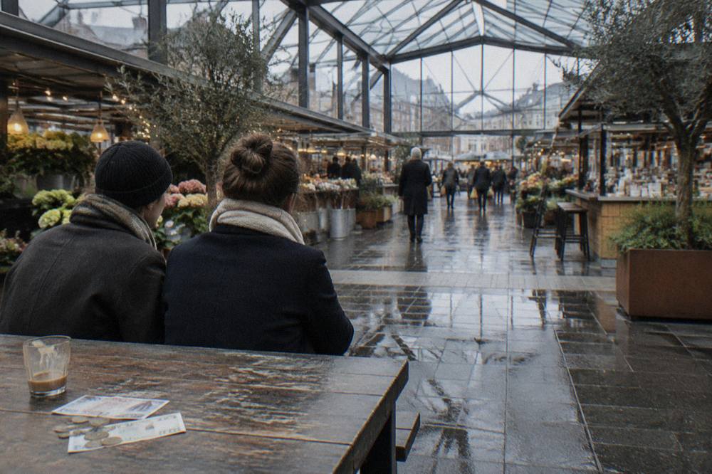 Two travellers counting Danish kroner notes together at a café table before a walking tour