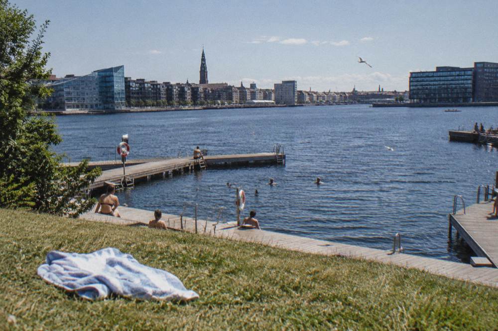 Wooden bathing jetties extending into a city harbour with a lawn along the waterfront