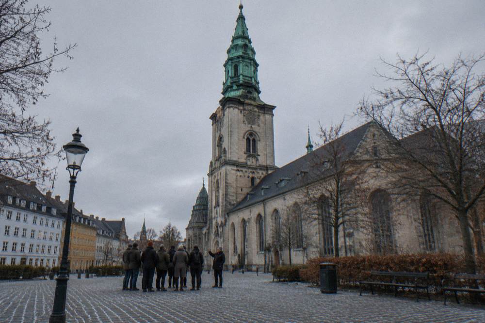 Un grupo pequeño de turistas escuchando a un guía frente a una iglesia antigua en el centro de Copenhague