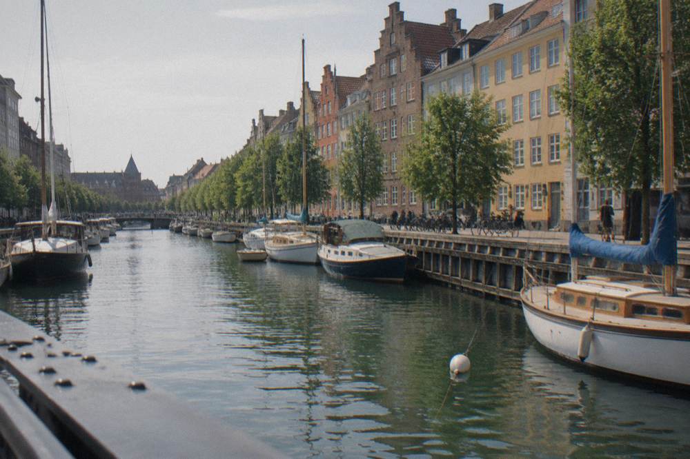 A canal with moored boats and coloured facades seen from a bridge