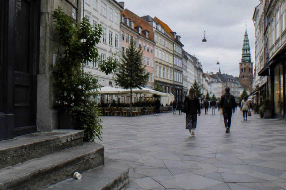 Calle del casco antiguo de Copenhague con fachadas pastel, ciclistas y peatones en una calle peatonal ancha