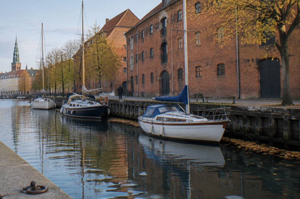 Narrow canal in Christianshavn lined with moored sailboats and old warehouse buildings