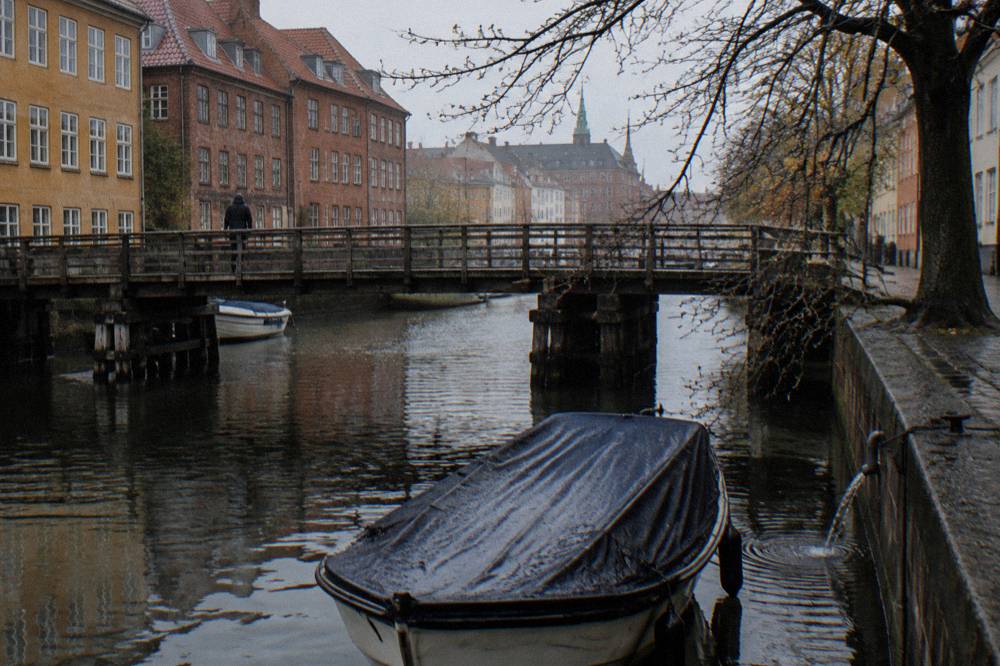 Un barco de canal amarrado junto a un puente de madera en Christianshavn, con árboles otoñales en la orilla