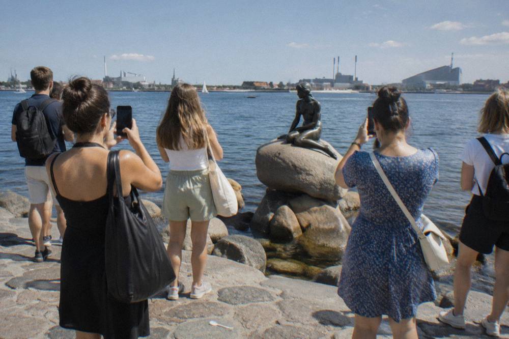 Visitantes reunidos en el paseo marítimo de Langelinie fotografiando la estatua de La Sirenita en su roca