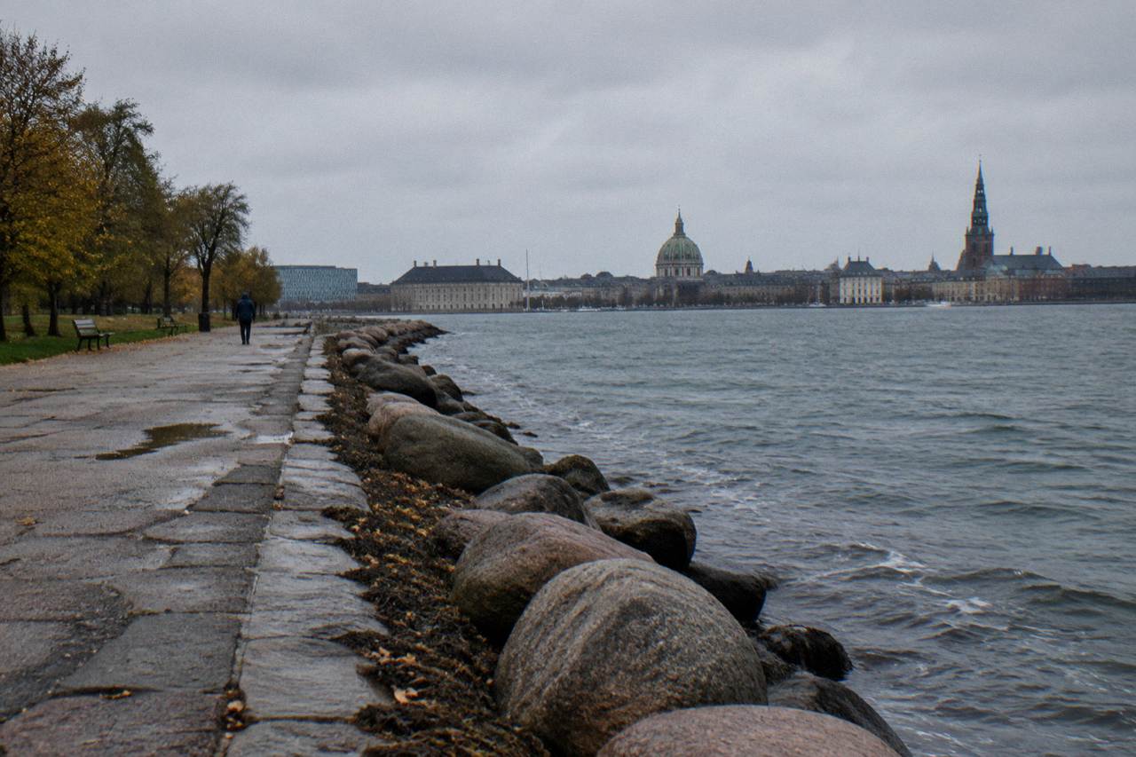 The Little Mermaid statue sitting on a rock at the water's edge in Copenhagen harbor