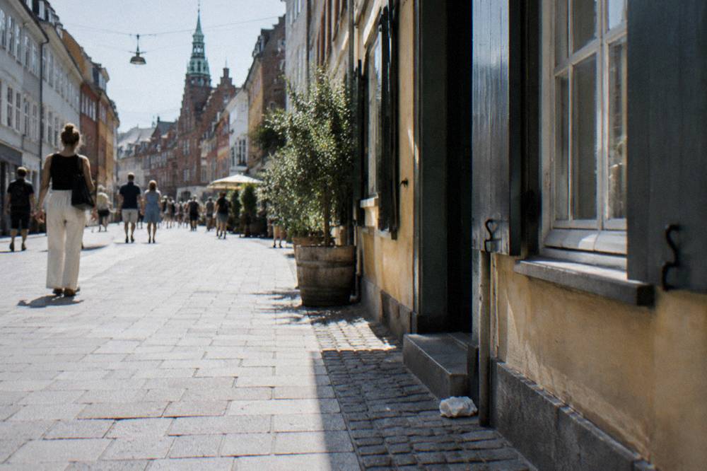 Visitors walking along a narrow cobbled street in Copenhagen's old town with colourful shopfronts