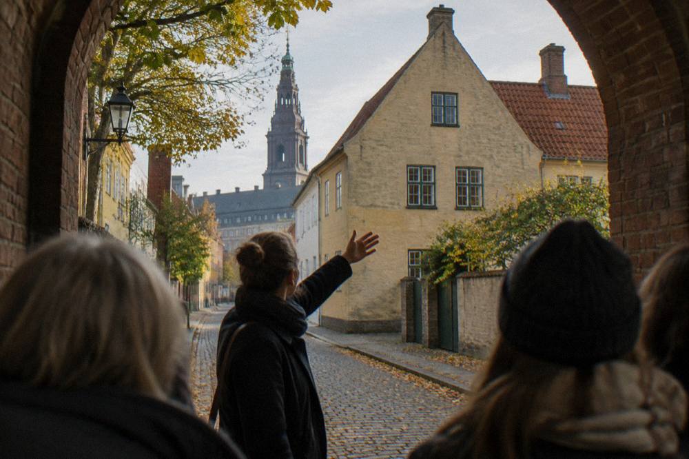 A guide pointing at a historic Copenhagen building while a small tour group listens on a narrow old street