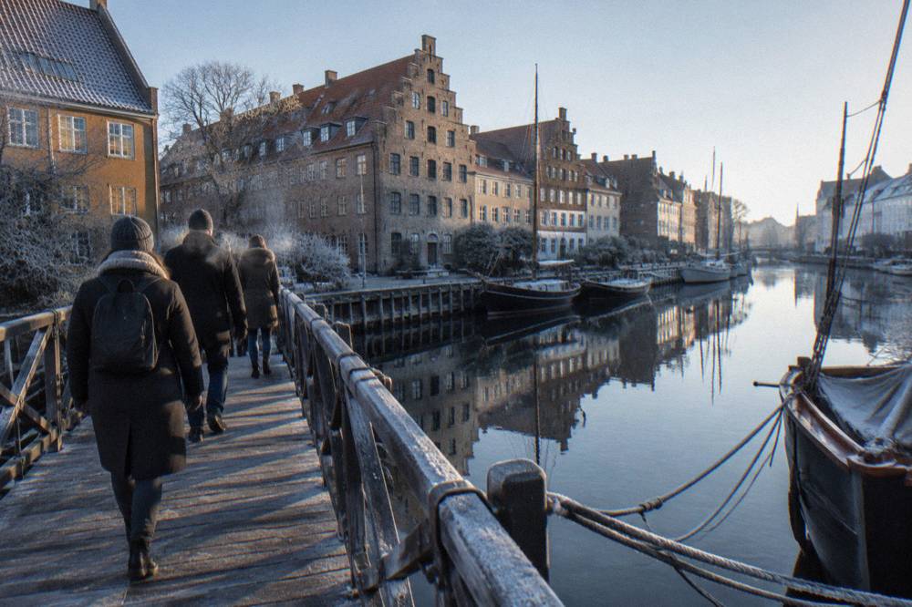 A small group of walkers with a guide crossing a Copenhagen canal bridge lined with old gabled facades