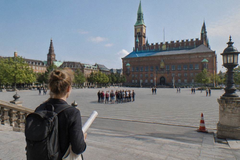 A tour guide holding up a map while visitors gather around on a Copenhagen square near the city hall