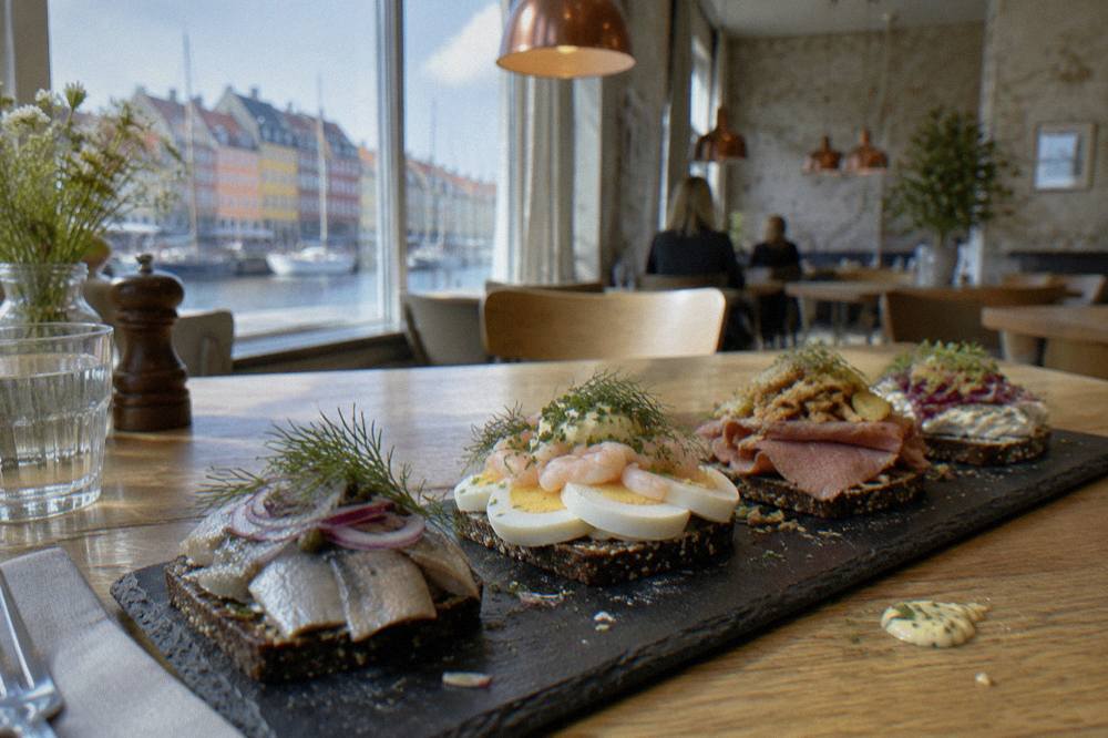 A row of open-faced sandwiches with herring, egg and roast beef toppings arranged on a slate board