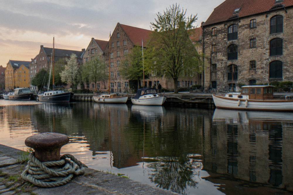 Canal boats moored along a Copenhagen waterway with old warehouses behind them
