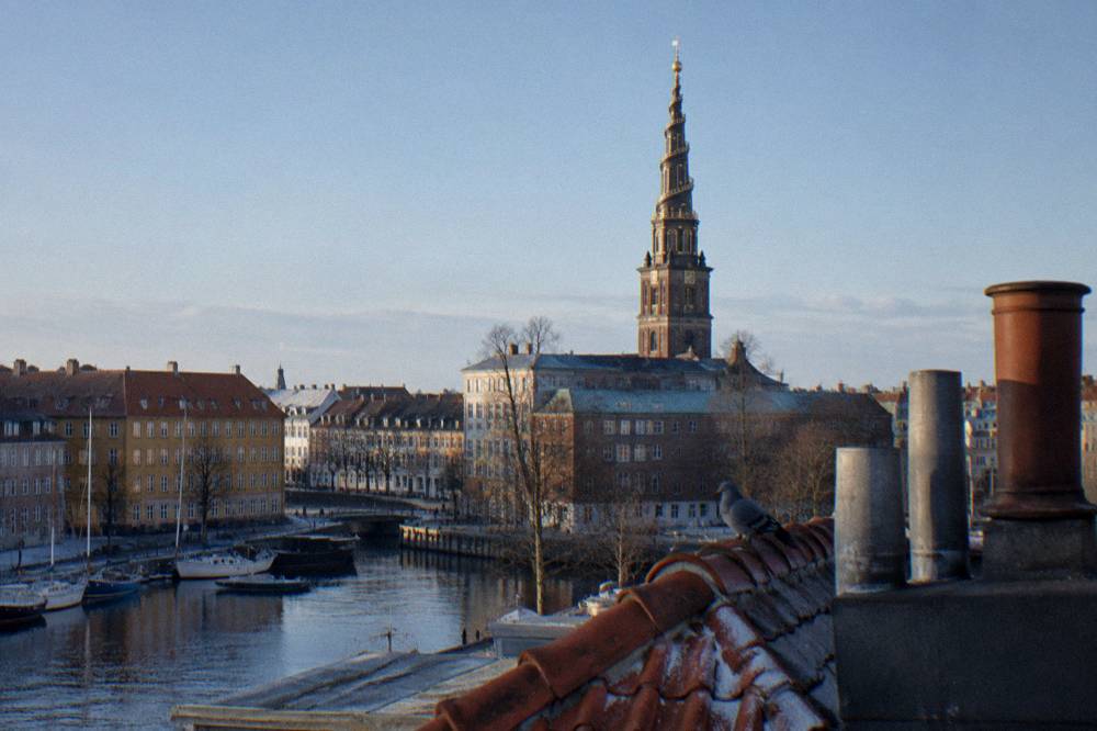 A church spire with an external spiral staircase seen from a city rooftop