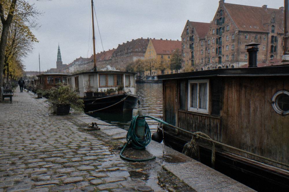 Wooden houseboats moored along a calm canal lined with old brick warehouses