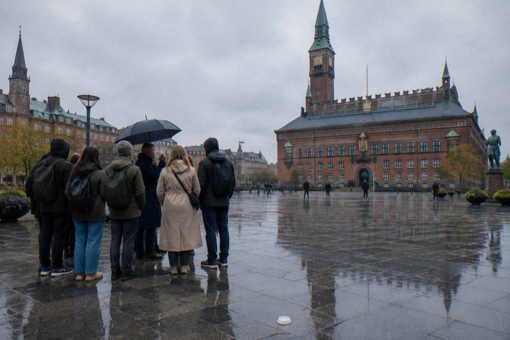 A Copenhagen square in the morning with a small group gathering near a guide holding a sign