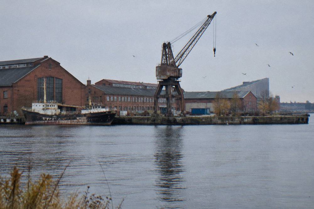 Old industrial shipyard buildings on a harbour island with calm water in the foreground