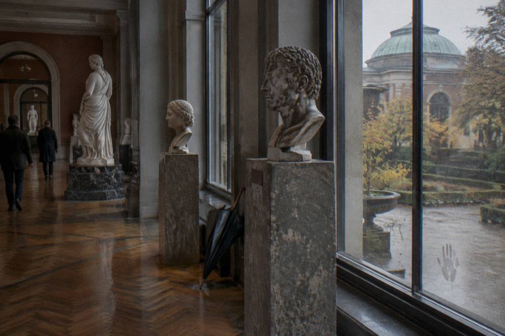 Museum gallery interior with marble sculptures lit by tall windows