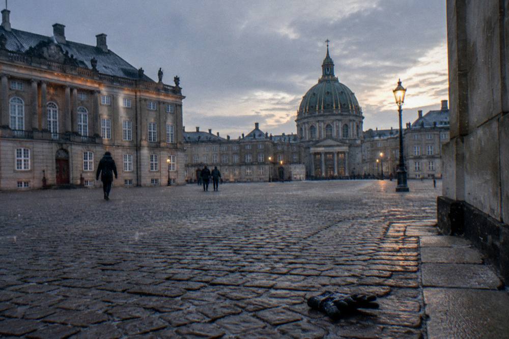 City square with a historic building facade and people walking on cobblestones
