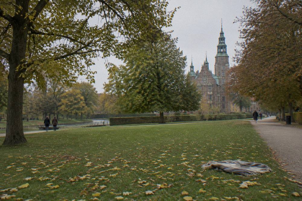 Wide green lawn with mature trees and a historic building visible beyond the edge of a city park