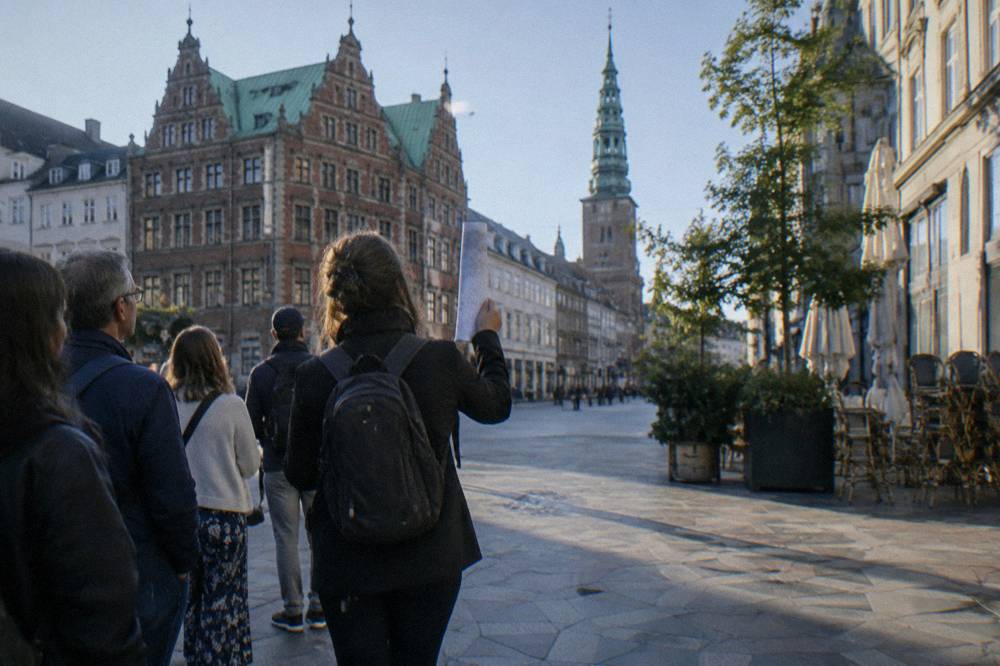 A local guide leading a small group of visitors on a walking tour through a Copenhagen city square