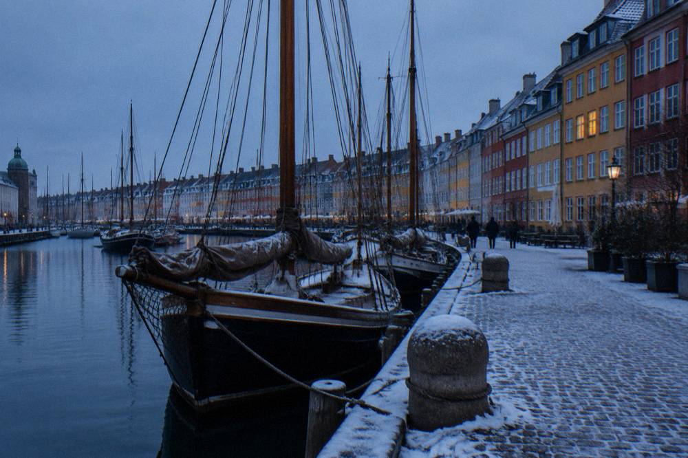 A colourful historic harbour street with wooden ships moored along the canal